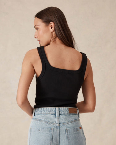 Woman wearing a black tank top and light blue jeans against a beige background